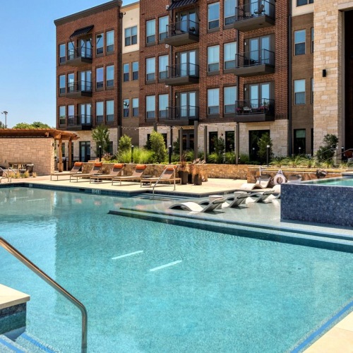 The pool area at our apartments for rent in Grapevine, TX, featuring lounge chairs and a view of the apartment exteriors.